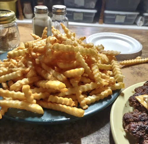 A large plate of crinkle-cut fries sits on a table next to a plate with a sandwich and condiments.