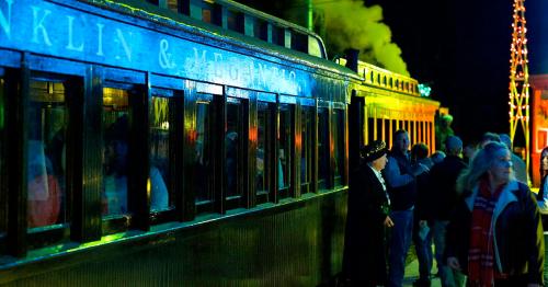 A vintage train station at night, illuminated with colorful lights and people gathered around.