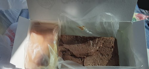 A box containing a piece of chocolate brownie and a small pastry, both wrapped in plastic.