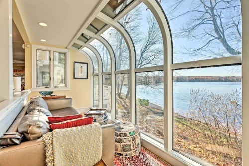 Cozy seating area with large arched windows overlooking a serene lake and trees in the background.