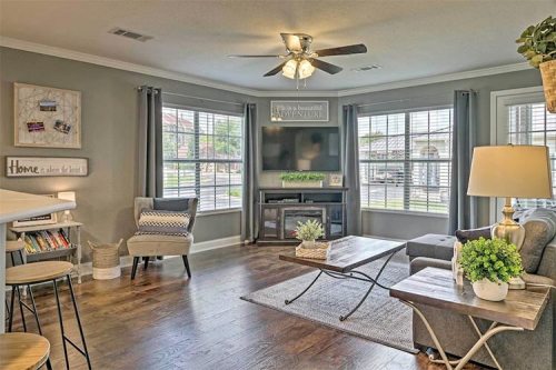 Cozy living room with a ceiling fan, large windows, a TV, and stylish furniture, featuring a warm, inviting atmosphere.