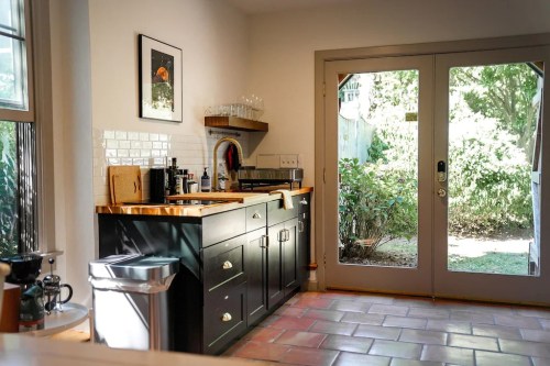 A bright kitchen with black cabinets, wooden countertops, and a view of a garden through glass doors.