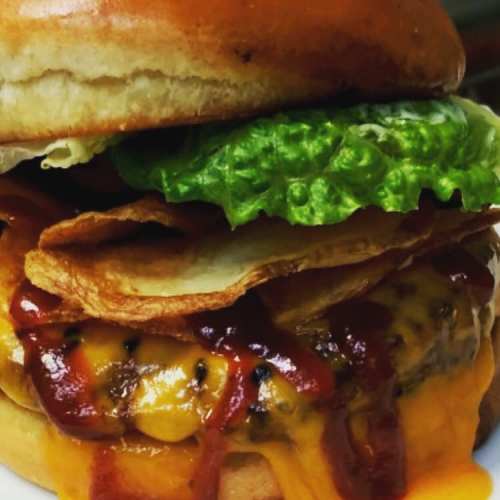 A close-up of a juicy cheeseburger with lettuce, crispy chips, and ketchup on a toasted bun.