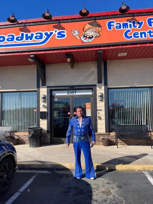 A person in a blue sequined outfit stands outside a family entertainment center with a colorful sign.