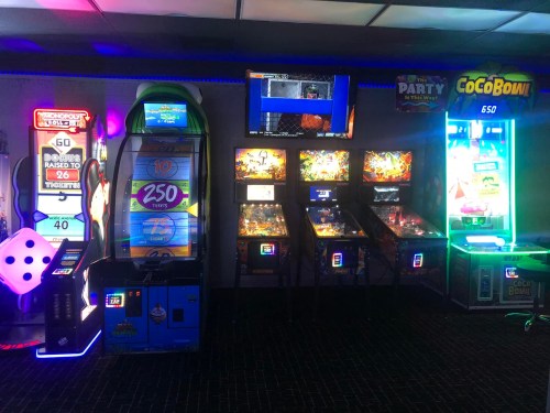 A brightly lit arcade featuring various games, including a ticket machine, pinball machines, and a prize redemption game.