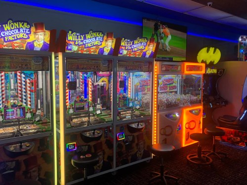 Colorful arcade machines themed after "Willy Wonka & the Chocolate Factory" with a sports game on a screen above.