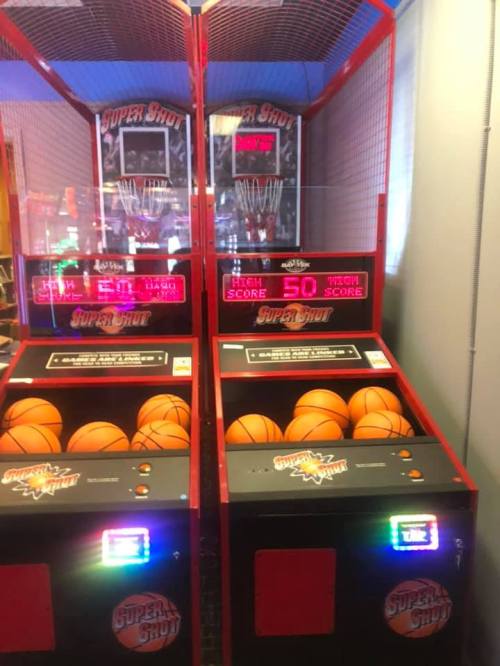 Two basketball arcade games with orange balls and score displays, set in a bright, fun environment.