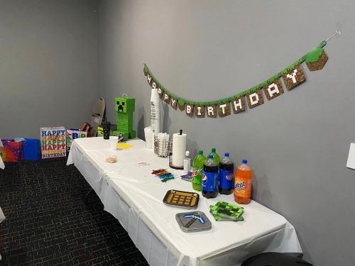 A birthday party setup with a "Happy Birthday" banner, snacks, drinks, and colorful decorations on a table.