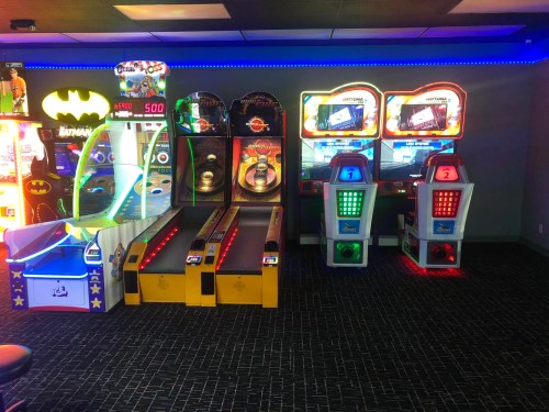 A colorful arcade room featuring various games, including basketball and racing machines, with vibrant lighting.
