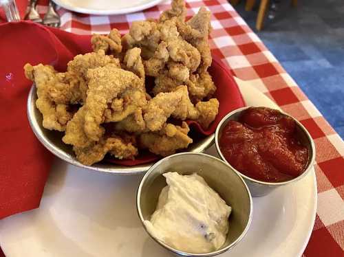 A plate of crispy fried food served with two dipping sauces: one red and one white, on a checkered tablecloth.