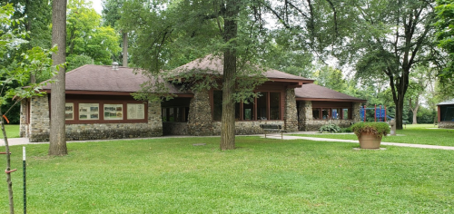 A stone building surrounded by trees and grass, with a pathway leading to it and a playground visible in the background.