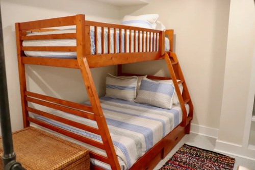 A wooden bunk bed with blue-striped bedding, a woven basket, and a colorful rug in a cozy room.