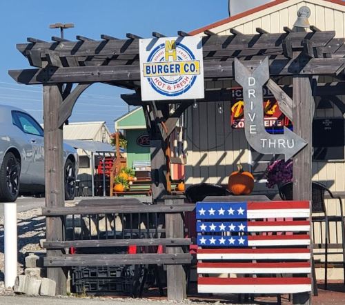 A wooden pergola with a sign for "Burger Co." and a drive-thru arrow, featuring an American flag decoration.