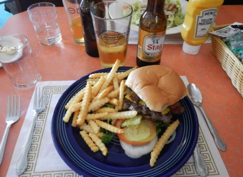 A plate with a burger, lettuce, tomato, and fries, accompanied by drinks on a table with a patterned tablecloth.