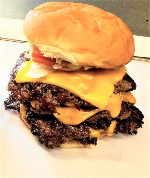 A towering cheeseburger with three beef patties, melted cheese, and fresh toppings, all in a soft bun.