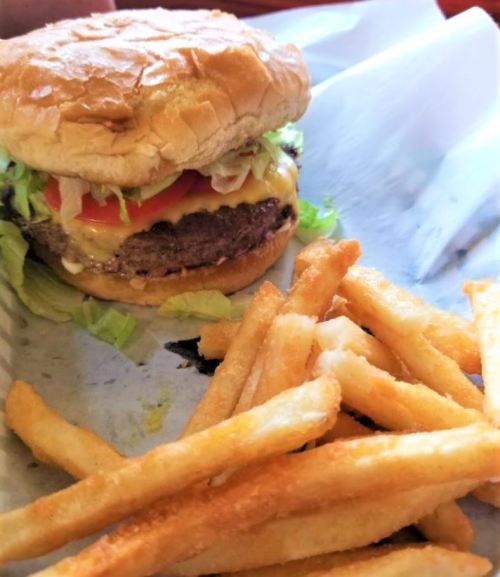 A close-up of a cheeseburger with lettuce and tomato, served with a side of golden French fries on a paper tray.