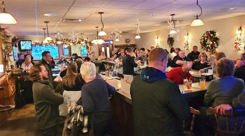 A busy bar decorated for the holidays, with patrons socializing and enjoying drinks at the counter.