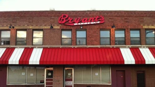 Exterior of Bryant's Barbeque, featuring a red awning and large sign, with windows reflecting the sky.
