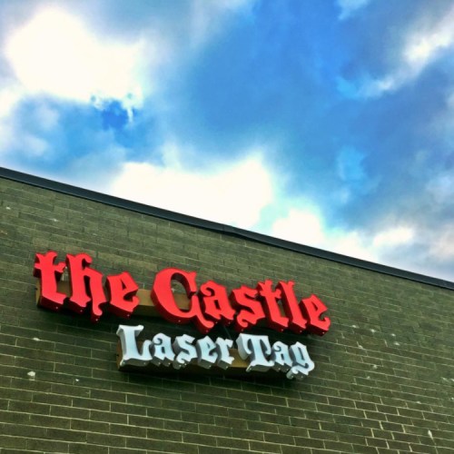 Sign on a building reading "the Castle Laser Tag" against a cloudy sky.