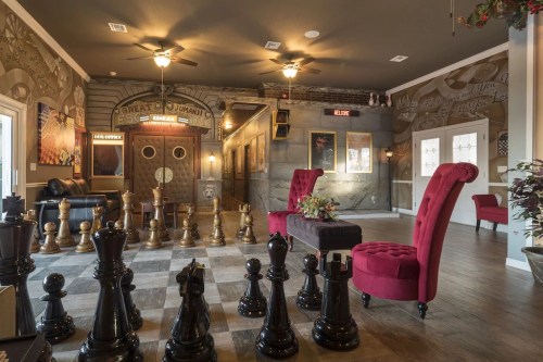 A stylish room with large chess pieces, elegant seating, and decorative walls featuring vintage-style artwork.