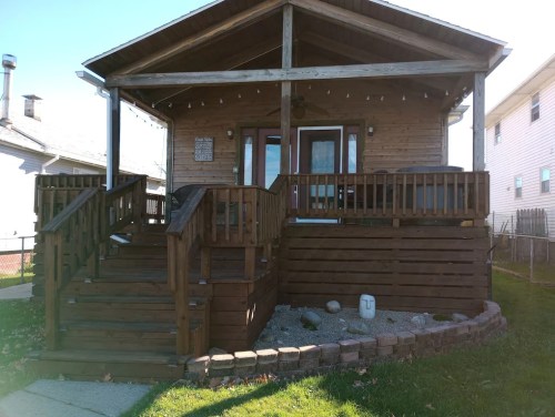 A wooden house with a porch, steps, and a landscaped yard, featuring a stone pathway and decorative elements.