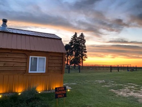 A cozy cabin at sunset, with a "Cabin Parking Only" sign and trees in the background against a colorful sky.