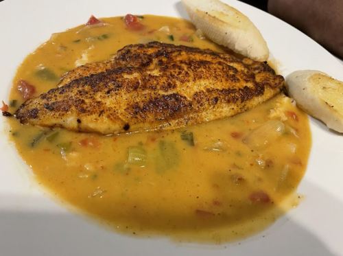 A seasoned fish fillet served in a creamy sauce with vegetables, accompanied by two slices of bread.