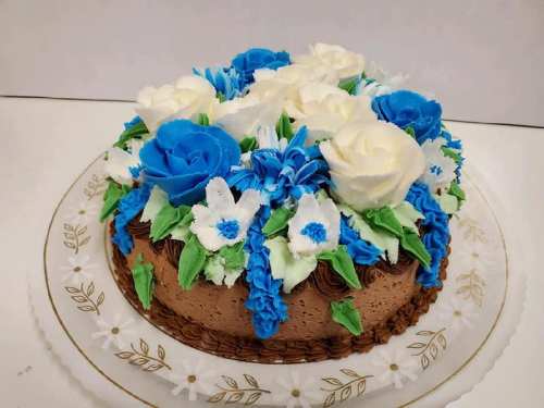 A round chocolate cake decorated with blue and white flowers and green leaves on a decorative plate.