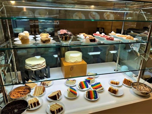 A display case filled with various cakes and desserts, including cupcakes, layered cakes, and colorful rainbow slices.