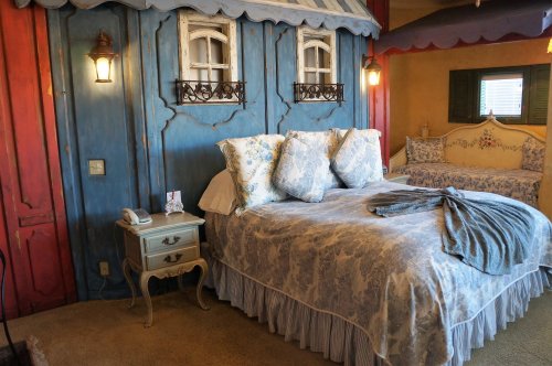 Cozy bedroom with a blue and red wall, floral bedding, and a small nightstand beside a bed.