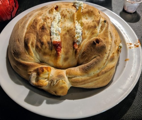 A large, golden-brown stuffed bread with visible filling, served on a white plate.