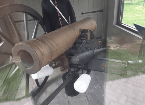 A historical cannon displayed indoors, with a person in period clothing standing beside it.