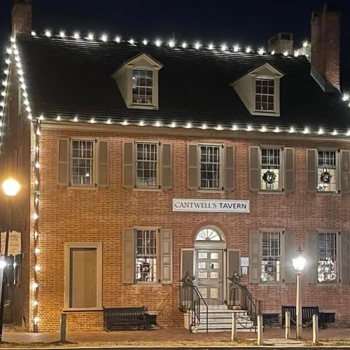 A historic brick building, Cantwell's Tavern, adorned with string lights at night.