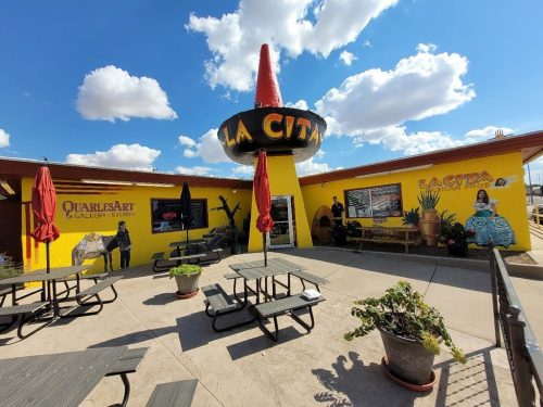 Colorful restaurant exterior with outdoor seating, vibrant murals, and a large sombrero sign against a blue sky.