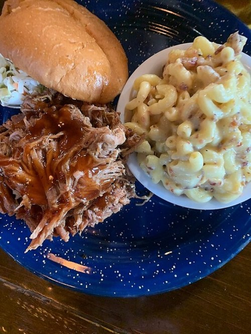 A plate featuring pulled pork with barbecue sauce, a bun, coleslaw, and creamy macaroni and cheese.