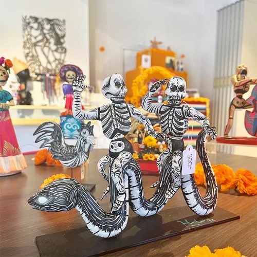 Colorful paper skeletons and a serpent figurine displayed with marigolds in a festive setting.