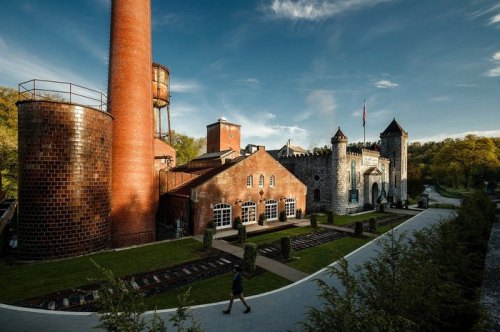 A scenic view of a castle-like building with a tall chimney and water tower, surrounded by greenery and pathways.