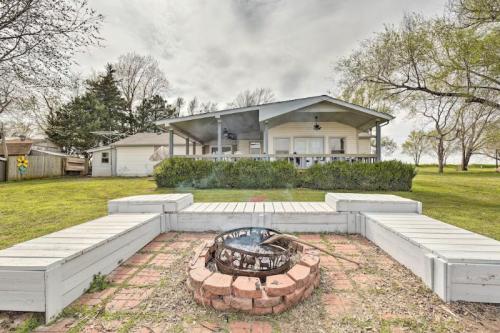 A cozy house with a porch, surrounded by greenery, and a fire pit in the foreground on a cloudy day.