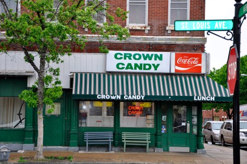 A storefront of Crown Candy with a green awning, featuring a Coca-Cola sign and benches outside.