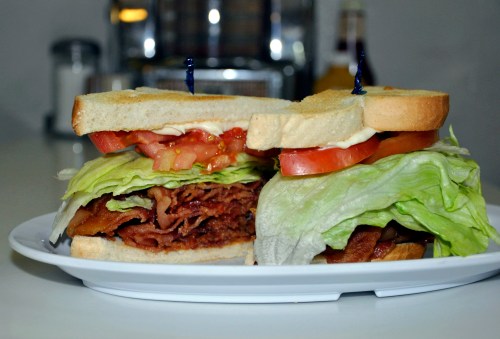 A large sandwich with layers of bacon, lettuce, tomato, and mayonnaise, served on white bread with toothpicks.