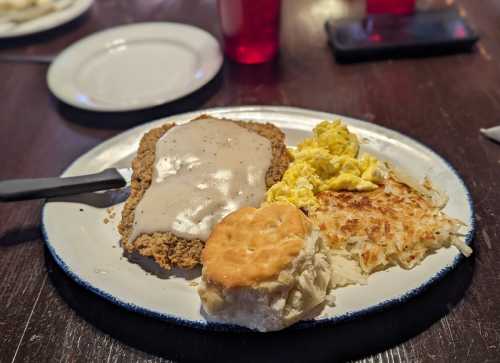 A plate with chicken fried steak topped with gravy, scrambled eggs, hash browns, and a biscuit.