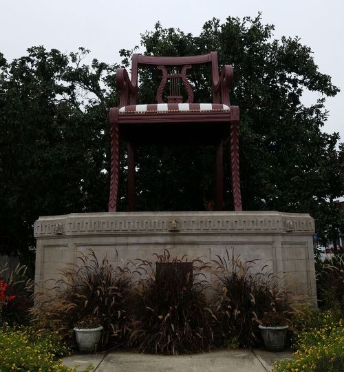 A large, decorative chair sculpture on a pedestal, surrounded by greenery and plants.