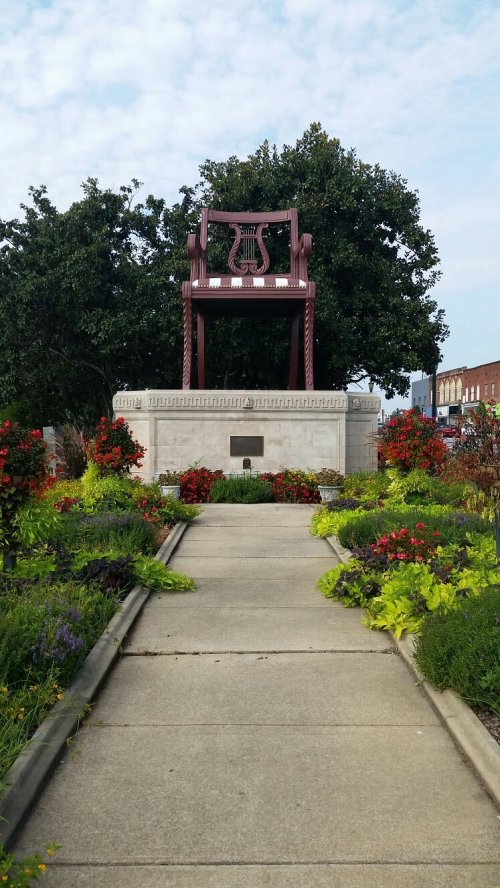 A large decorative chair sculpture surrounded by colorful flowers and greenery in a park setting.