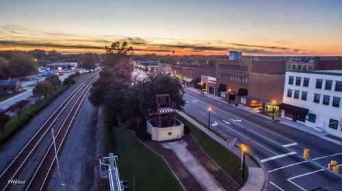 Aerial view of a quiet town at sunset, featuring train tracks, buildings, and a tree-lined street.