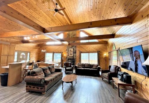 Cozy wooden living room with high ceilings, large windows, and comfortable seating.