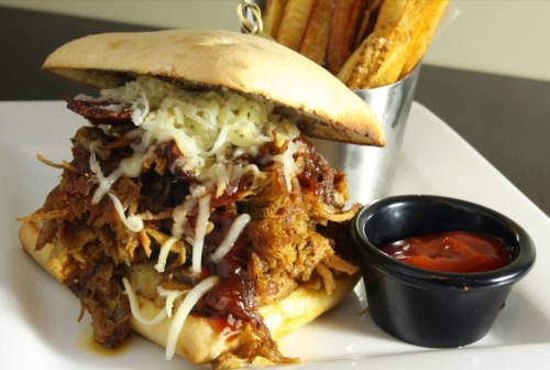 A hearty pulled pork sandwich topped with cheese, served with fries and a side of barbecue sauce.