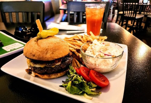 A juicy burger with cheese, lettuce, and tomato, served with fries, coleslaw, and a drink in a casual dining setting.