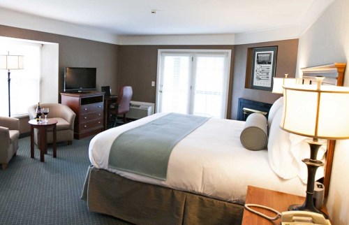 A cozy hotel room featuring a king bed, seating area, TV, and large windows with natural light.