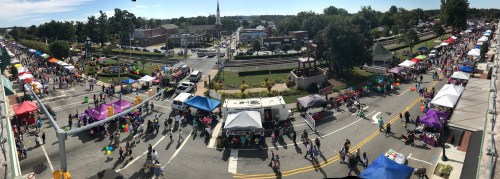 Aerial view of a bustling street fair with colorful tents, vendors, and crowds enjoying the festivities.