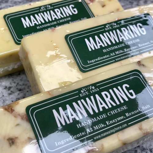Two blocks of handmade cheese with green labels displaying the brand "Manwaring" and ingredient details.